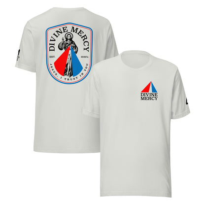 A silver short-sleeve T-shirt shown from both the front and back. The front features a red and blue triangular Divine Mercy logo with black text on the left chest. The back features a modern logo of the Divine Mercy image. Catholic Clothing.